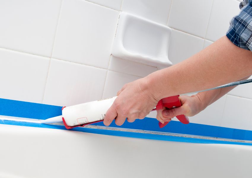 contractor using white caulk to fix bathroom shower grout